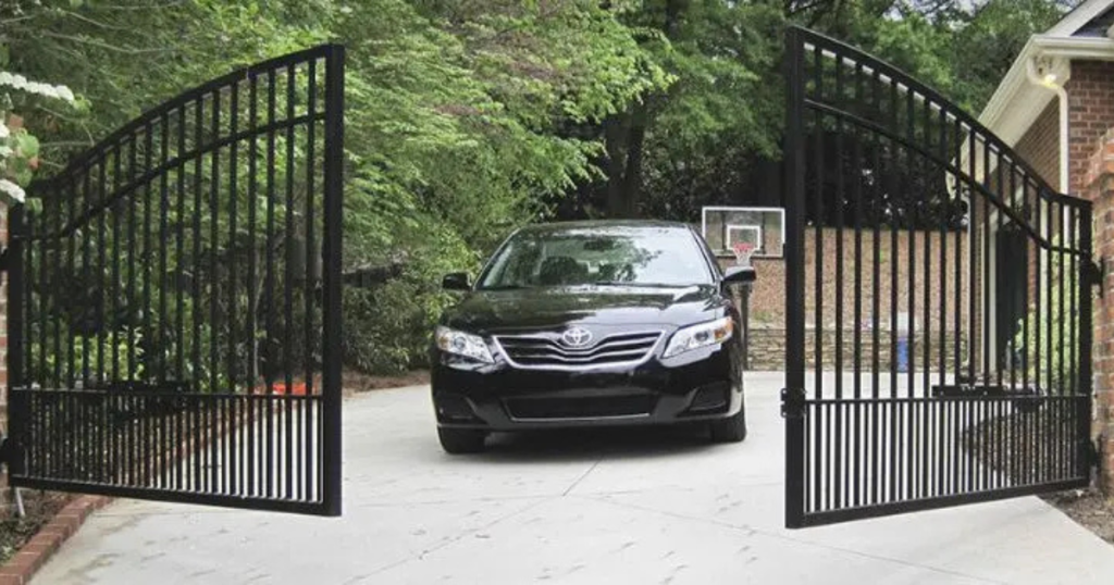 Black car driving through an open wrought iron gate.
