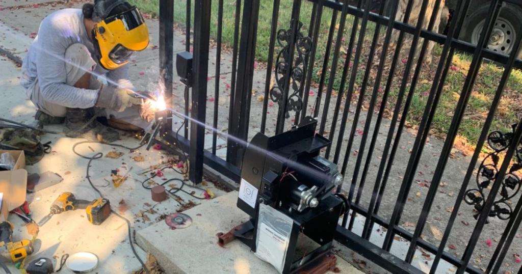 Worker welding a gate with a motorized gate opener.