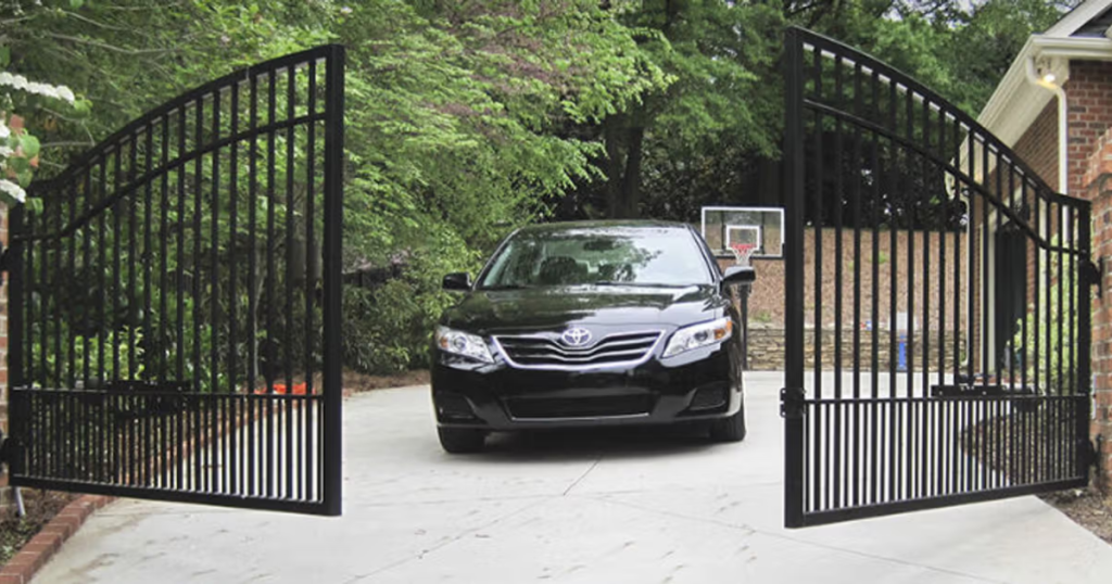 Black car driving through open metal gates.